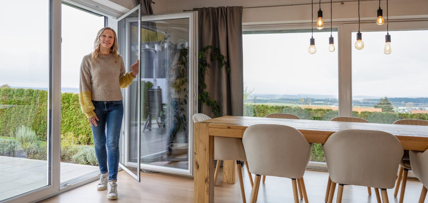 Frau mit braunen Haaren steht am offenen Fenster und setzt einen Spannrahmen ein.